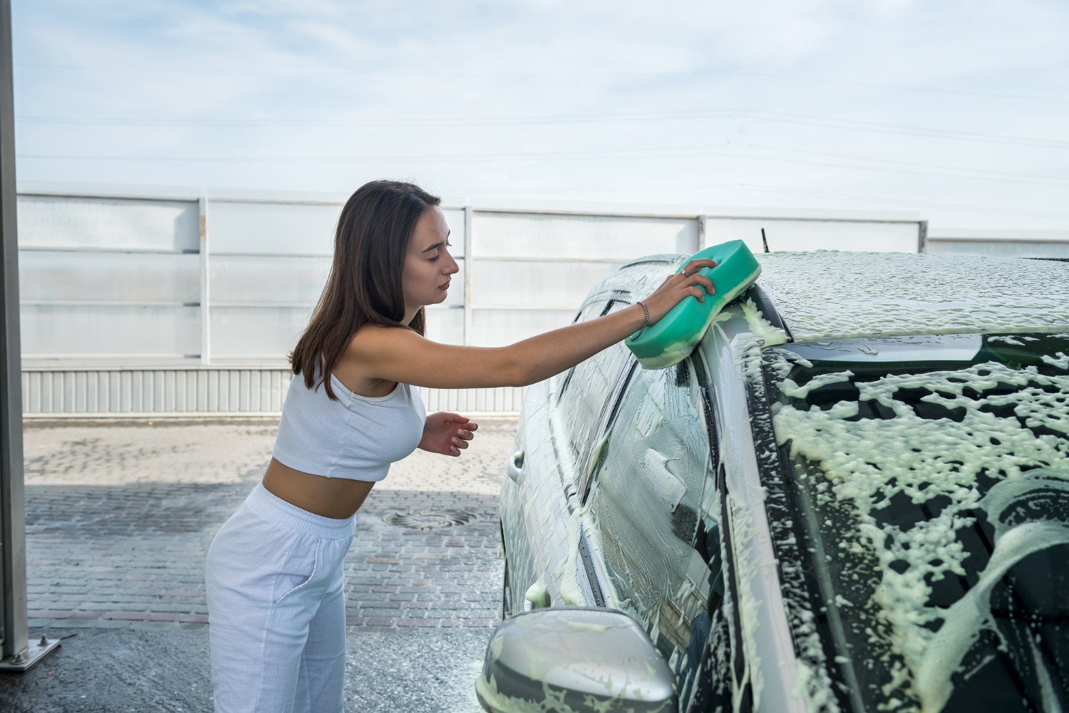 pretty female driver wash foam with green sponge cleaning her car from dirty
